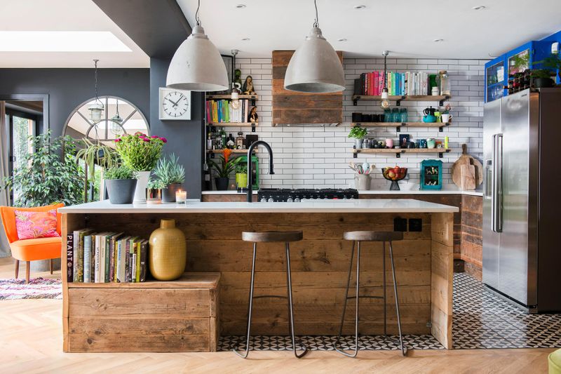 A modern kitchen with rustic wood accents. Books are stored in the kitchen island and on open shelving bringing a pop of color to the room. 