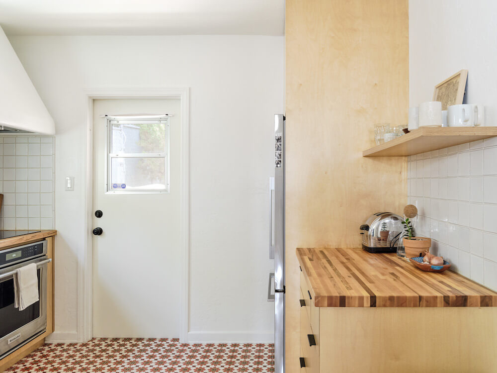 Kitchen with plywood cabinets, Moroccan floor tiles, open shelving and white wall tile