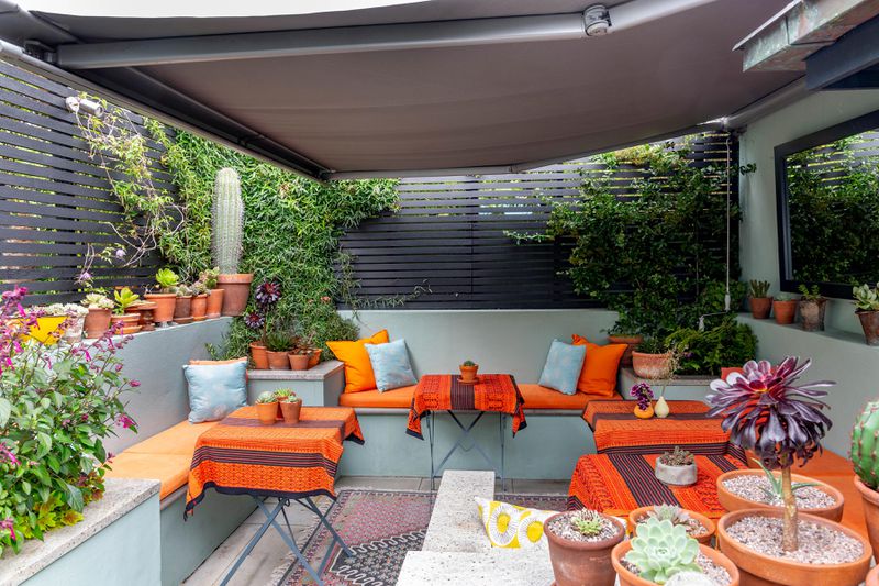 An outdoor sitting area with orange accents and a gray fabric canopy overhead. 