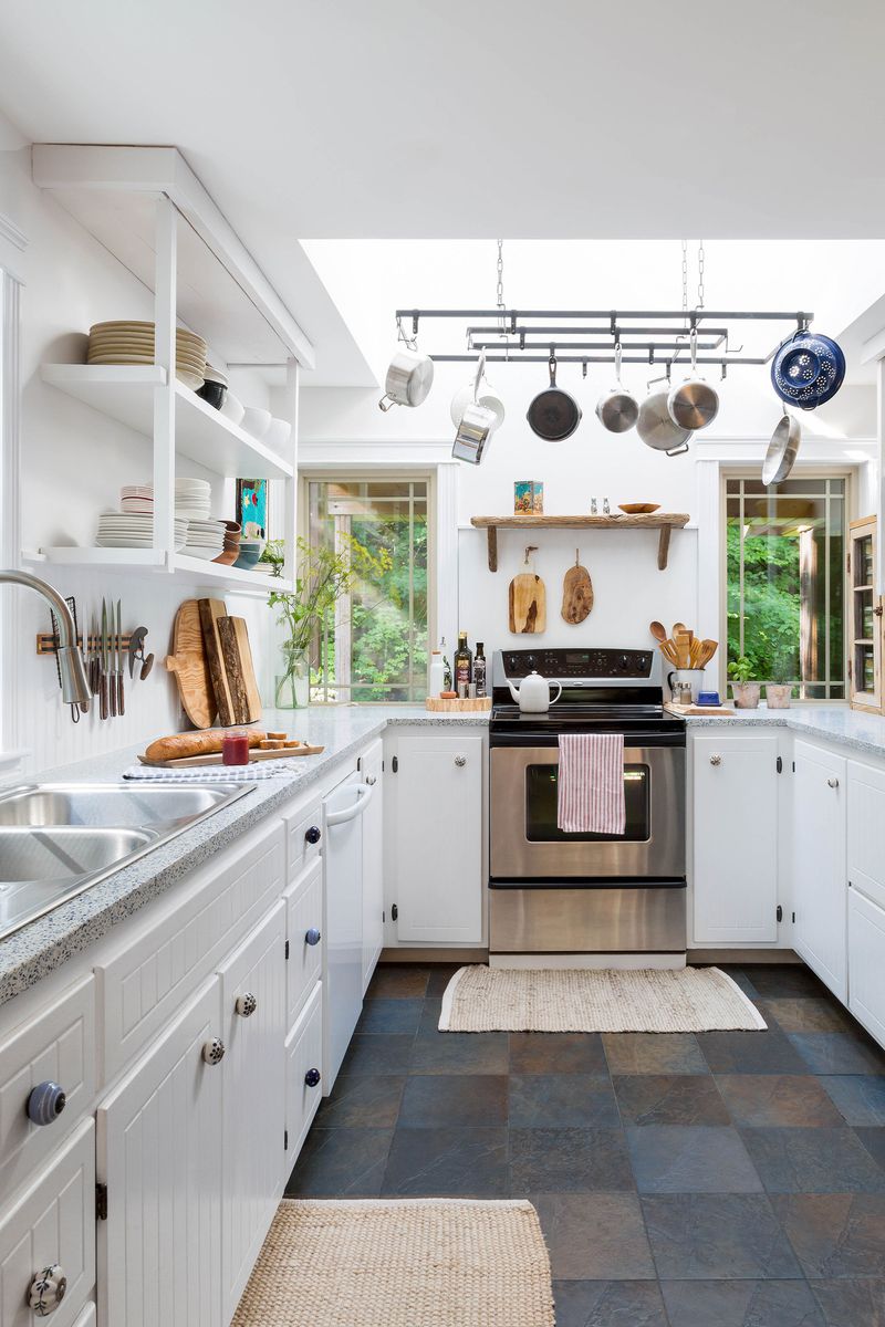 A gallery kitchen with several storage solutions including open shelving, magnetic wall mounts for knives and an overhead pot rack. 