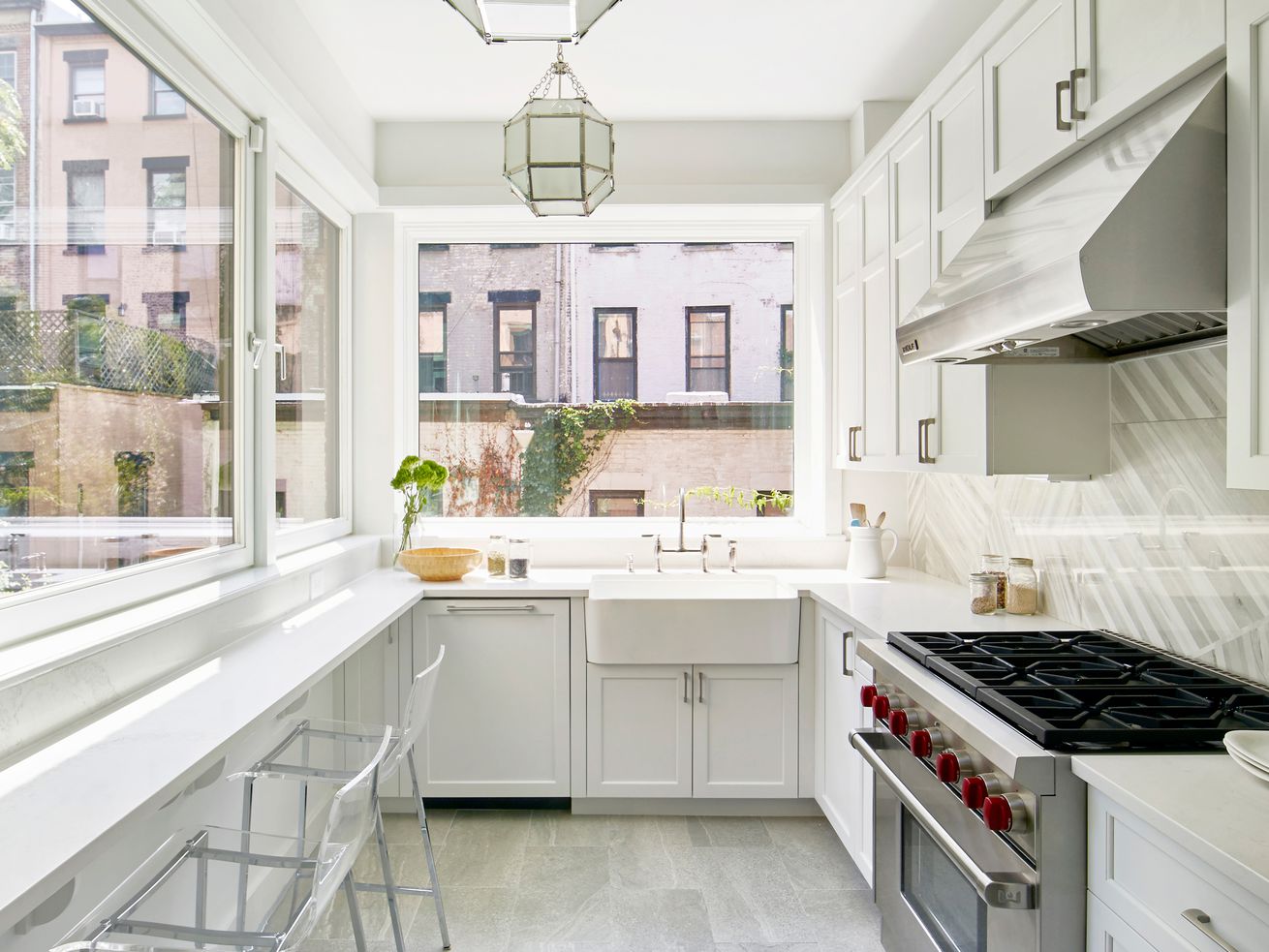 A white galley kitchen with large windows on two sides, as well as pendant lights down the length of the room.