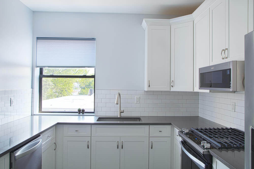 Image of a small kitchen area with white cabinets and white subway tile walls