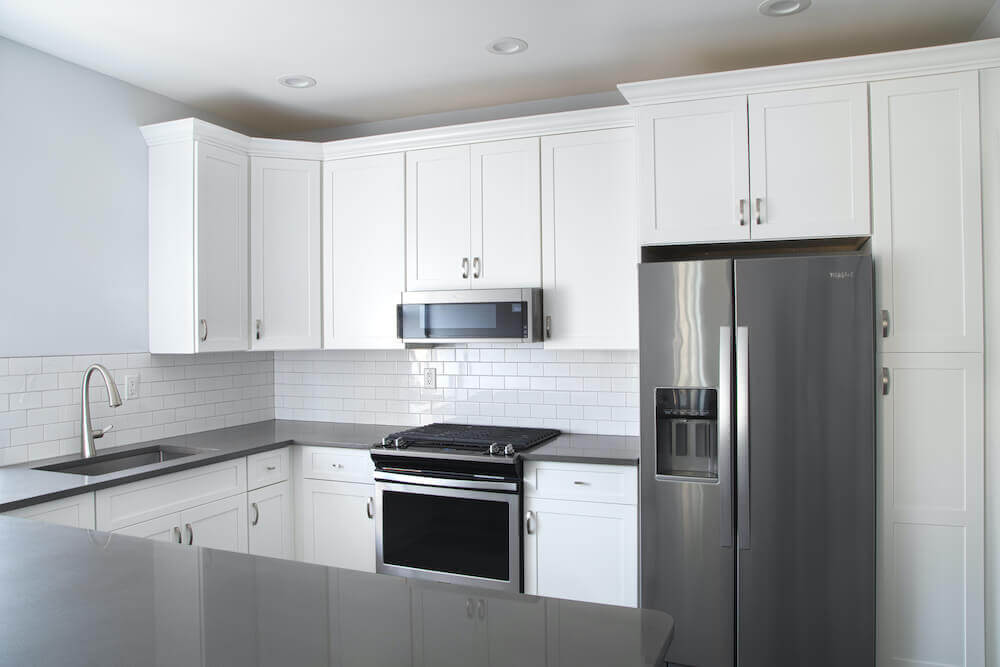 Image of a renovated white kitchen with gray countertops and silver fridge