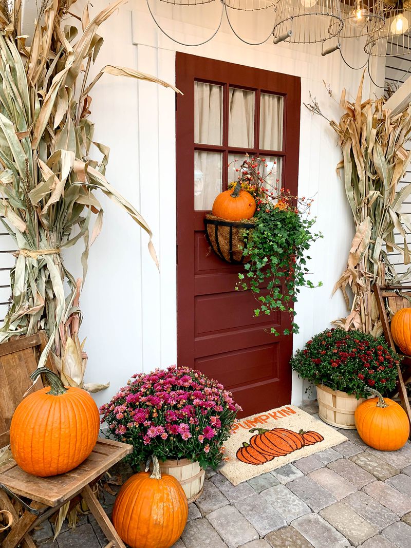 A front door with fall decor including mums in apple crates, pumpkins and dried corn stalks. 