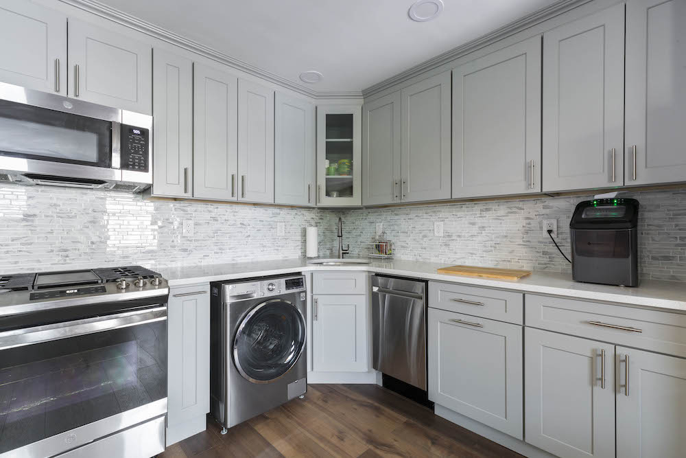 Light gray kitchen with gray backsplash along with closed cabinet and stainless steel appliances after renovation