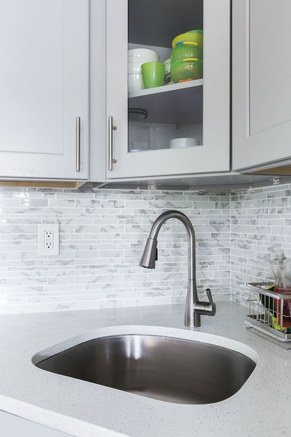 Light gray kitchen cabinets with gray countertop along a gray backsplash and small sink after renovation
