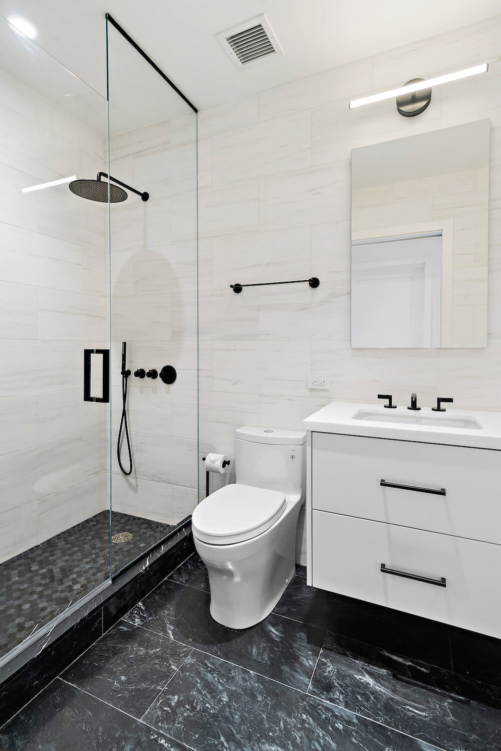 Small white bathroom with glass separator for walk-in shower along with floating vanity over black floor tile