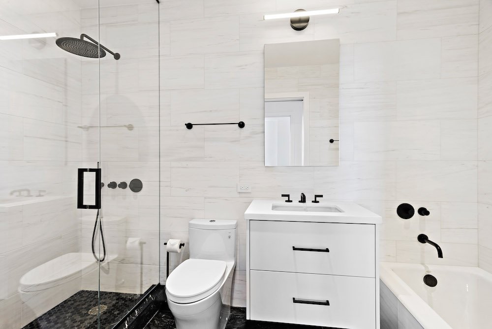 Small white bathroom with glass separator for walk-in shower and bathroom vanity with mirror after renovation