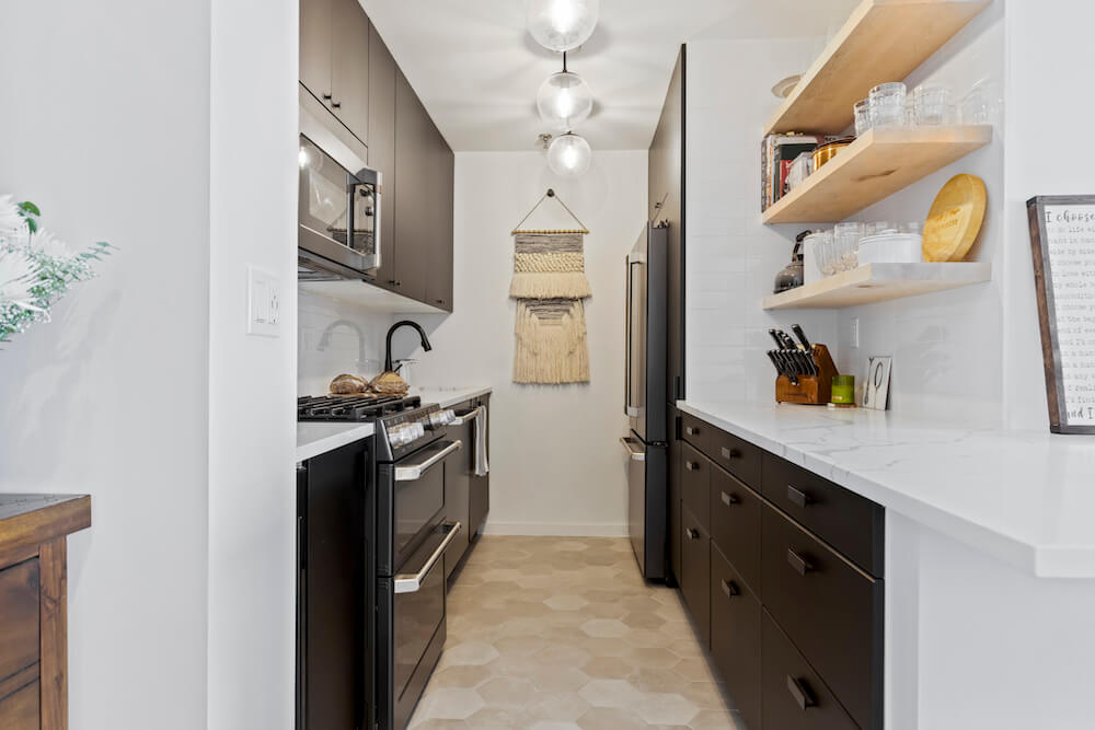 Renovated kitchen with beige tile, black cabinets, and white marble counter