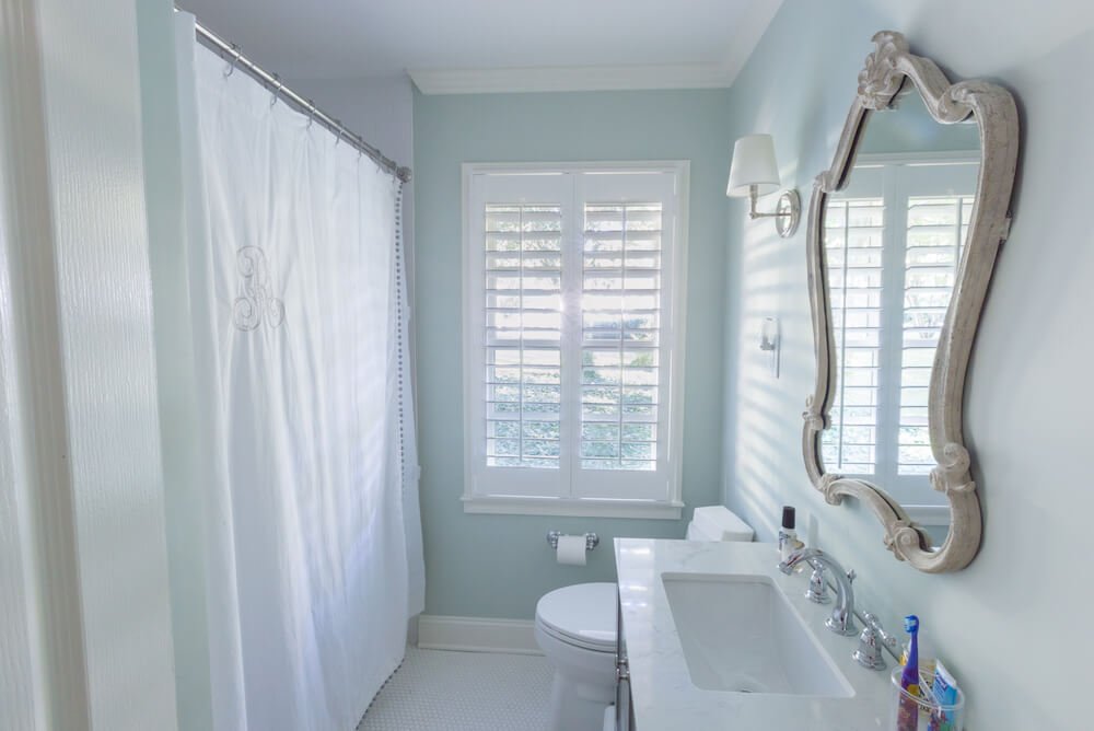 Bathroom with light blue walls, white floors, white shower curtain, and decorative mirror