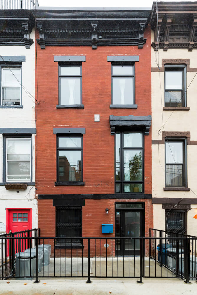 Image of the exterior of a red brick rowhouse with black windows in the South Brox