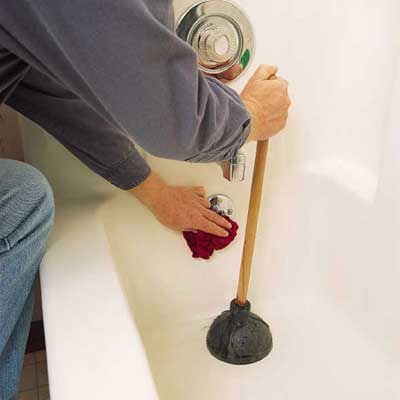 Person using a plunger on a clogged bathtub drain.