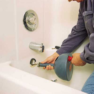Person cutting through a clog in a bathtub with a cable also known as plumber’s snake.