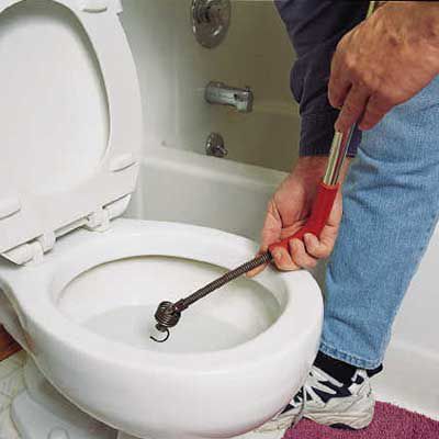 Person using a closet auger in a toilet bowl to clear a clog.