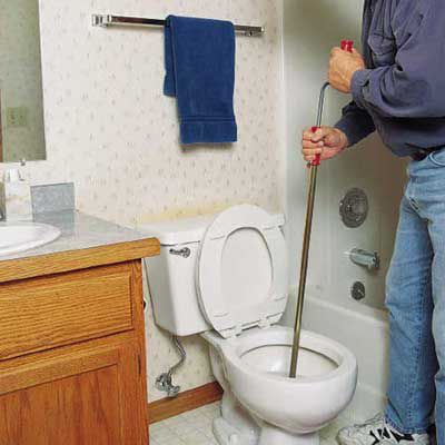 Person using a crank in the toilet bowl to clear a clog.