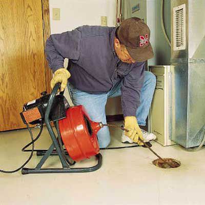 Person using a power auger to clear a floor drain.