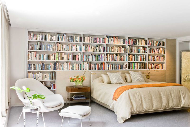 A modern bedroom with a wall of bookshelves behind the bed. 