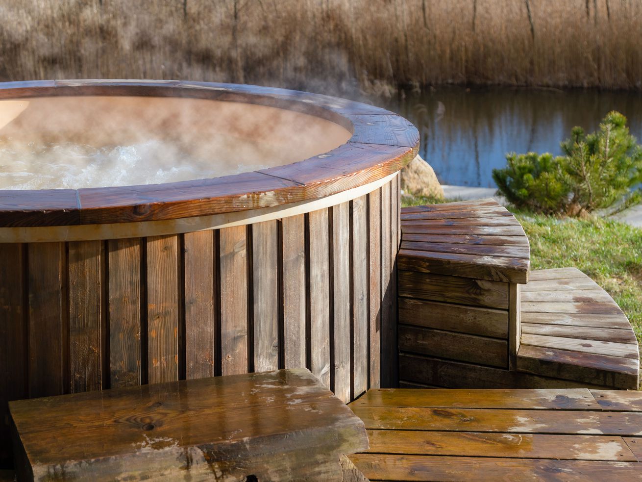 A round, wooden hot tub bubbles and steams next to a wet deck. 