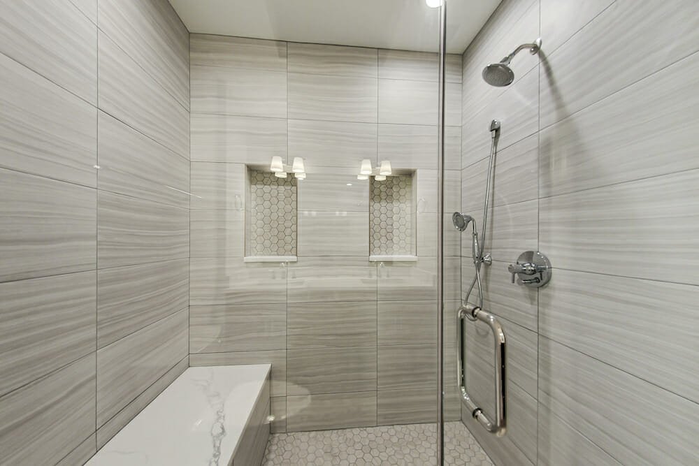 walk-in shower with bench and marble tiles on walls and recessed shelves and glass door after renovation