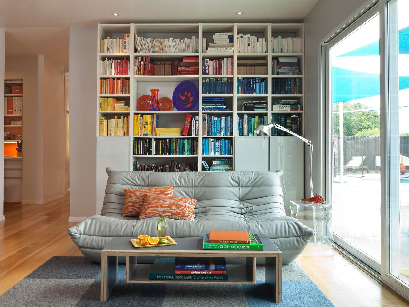 A modern living room with a library full of books that are color coordinated in a rainbow spectrum.