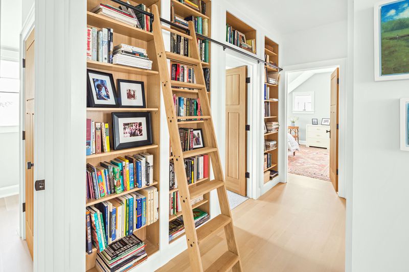 A library in the hallway of a home, equipped with a ladder that allows you to get books from the upper shelves. 